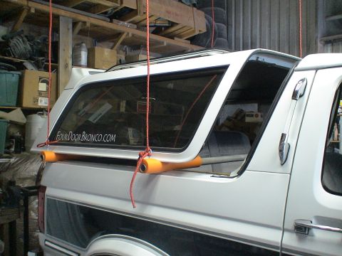 1993 Ford C-350 (Centurion Conversions) - A white pickup truck's camper shell is suspended by ropes, with orange padding underneath.