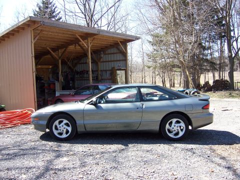 1996 Ford Probe - A gray 1996 Ford Probe is parked next to a red car under an open-sided carport.