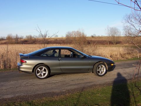 1996 Ford Probe - Side profile of a gray 1996 Ford Probe coupe parked on a dirt road with a field in the background.