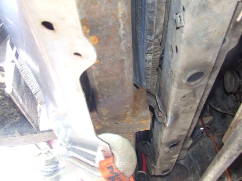 1986 Ford Bronco - Tight overhead shot down into an engine bay under repair, showing a surface-rusted frame or core-support crossmember beside a radiator core…