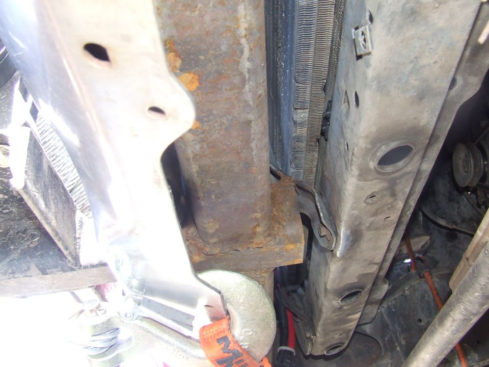Rusty frame crossmember and radiator in a stripped engine bay with a grinder resting nearby