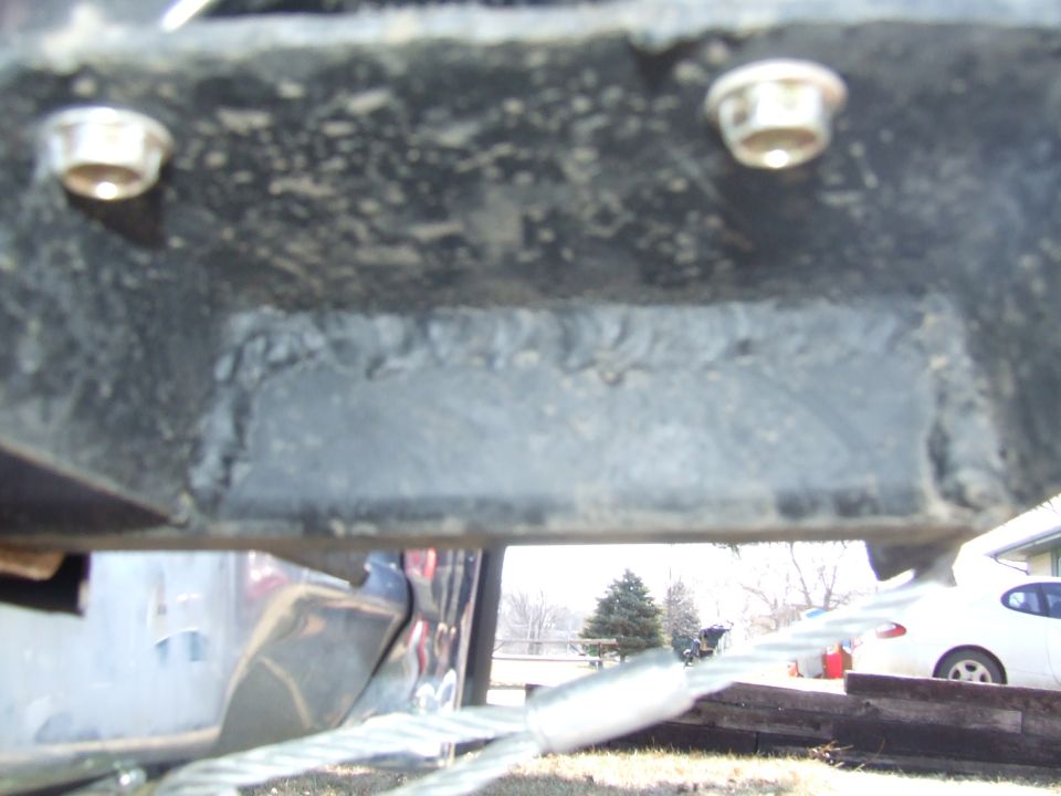 Close-up of welded reinforcement plate and bolts on a black steel frame rail with winch cable