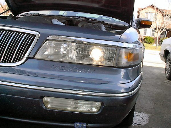 Dark blue Mercury Grand Marquis front end with hood open, showing chrome grille and headlight