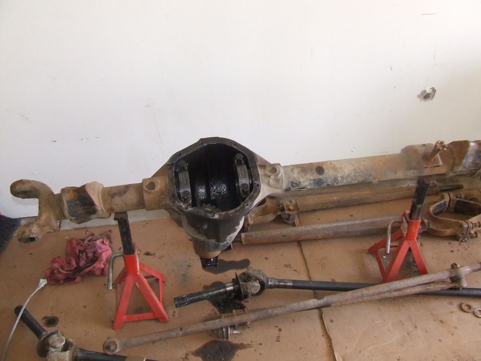 Front axle housing on red jack stands with differential open, axle shafts and steering parts on garage floor