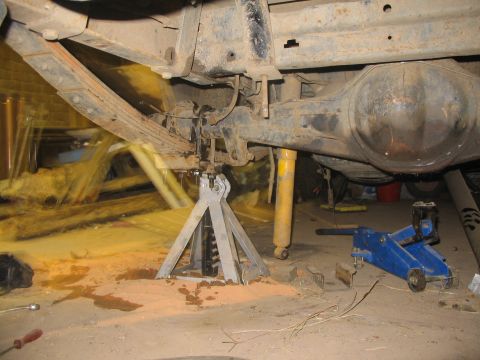 1981 Ford Bronco - The rear axle assembly of a vehicle is supported by jack stands and a hydraulic jack, with visible leaf springs and shock absorbers.
