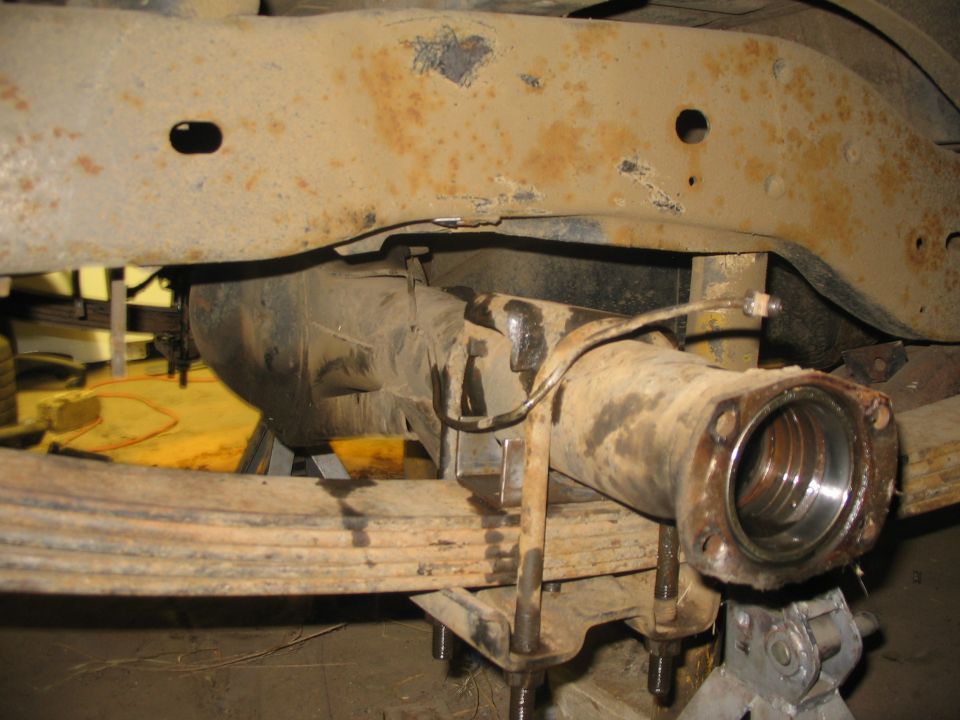 Close-up of a vehicle's rear axle assembly and leaf springs, showing rust on the frame