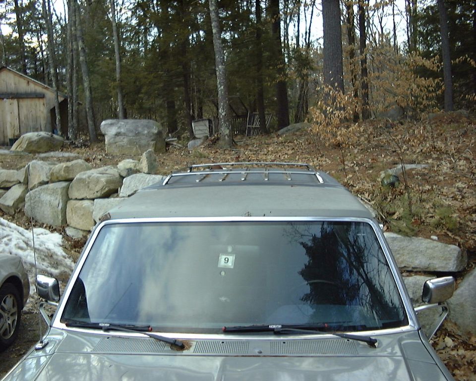 Front view over hood of gray SUV with roof rack, windshield sticker '9', parked among boulders and trees