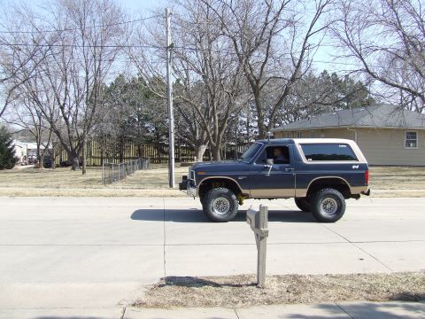1986 Ford Bronco - A two-tone Ford Bronco is seen driving down a residential street on a clear day.