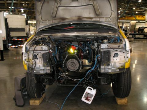 1993 Ford Bronco - Van front end disassembled, engine bay exposed, with a jug of fluid on the ground.