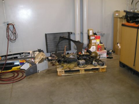 1993 Ford Bronco - Various vehicle parts, including an engine, radiator, and grille, are organized on a pallet in a workshop.
