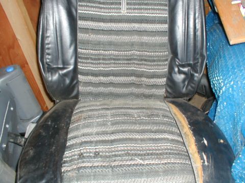 1979 Ford Bronco - Interior view of a damaged car seat with striped fabric and black vinyl trim.