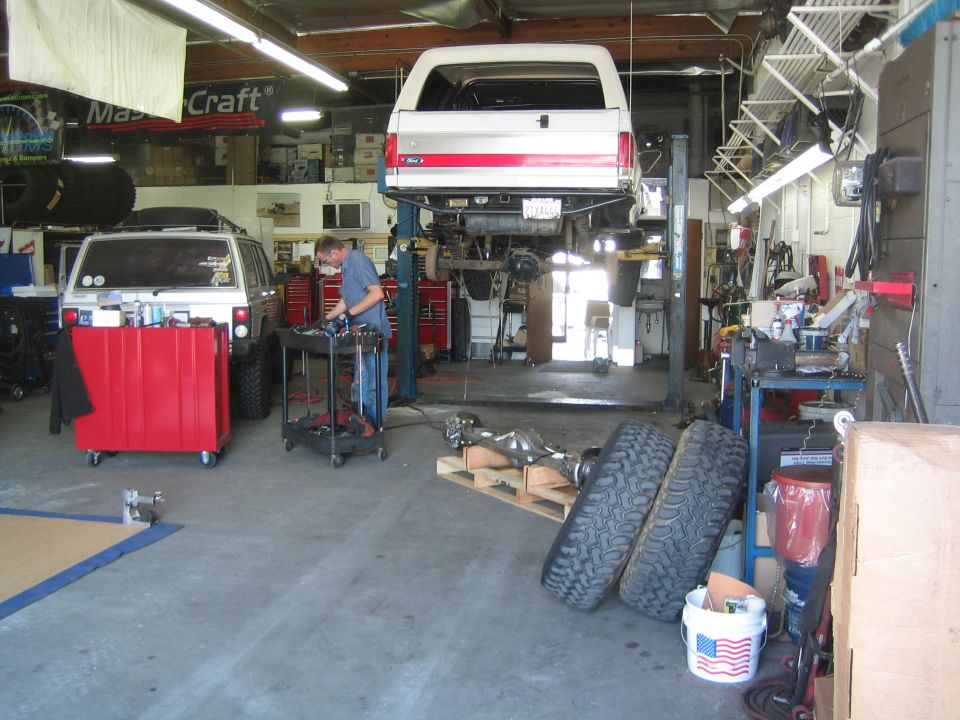 Repair shop interior with a Bronco on a lift, tool carts, tires and a red toolbox
