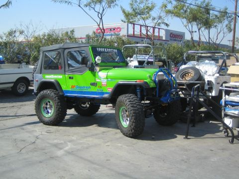 1990 Ford Bronco - lifted green Jeep Wrangler on off-road tires sits in a parking lot with a Costco warehouse in the background.