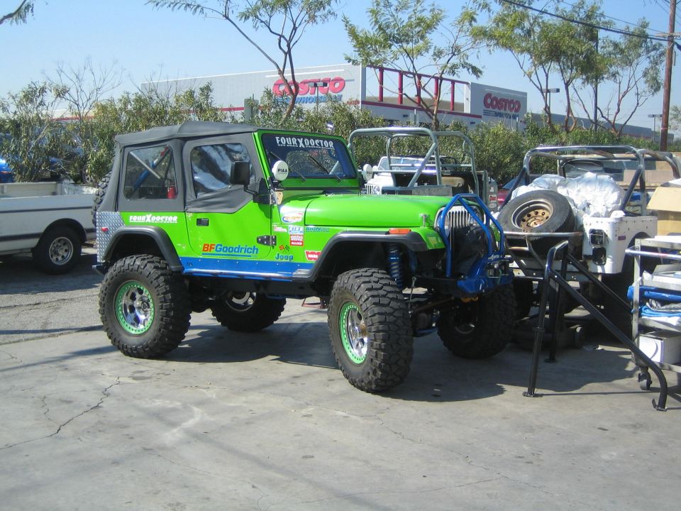 Lifted green Jeep Wrangler with off-road tires parked in a lot near a Costco store