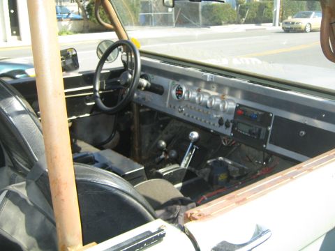 1990 Ford Bronco - Interior of an open-top off-road vehicle with steering wheel, aftermarket gauges, twin shifters and a padded roll-cage bar.