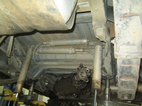 1990 Ford Bronco - Undercarriage view of a vehicle on a lift showing the driveshaft, transfer case and steering linkage.