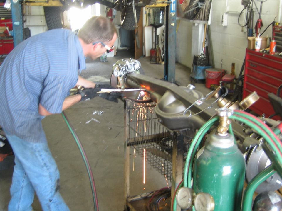 Man in blue shirt using a torch to cut or weld an axle housing on a shop cart