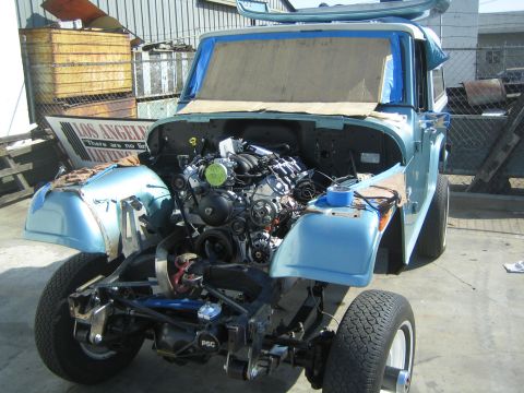 1990 Ford Bronco - light blue vintage 4x4 sits in a yard mid-build with its hood removed, exposing a fresh V8 swap and the front suspension and frame.
