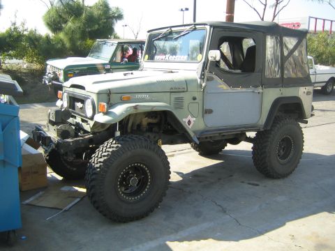 1990 Ford Bronco - sage green Toyota Land Cruiser FJ40 with a soft top and oversized off-road tires sits on pavement with another FJ40 behind it.