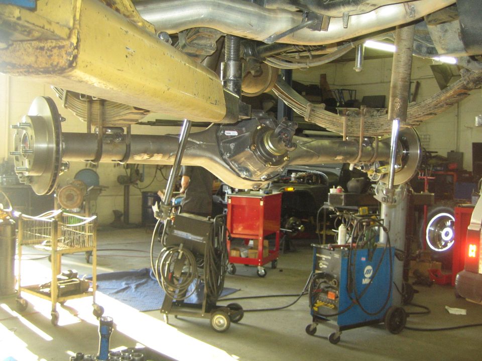 Vehicle underside on lift showing driveshaft, differential and axle in a busy shop
