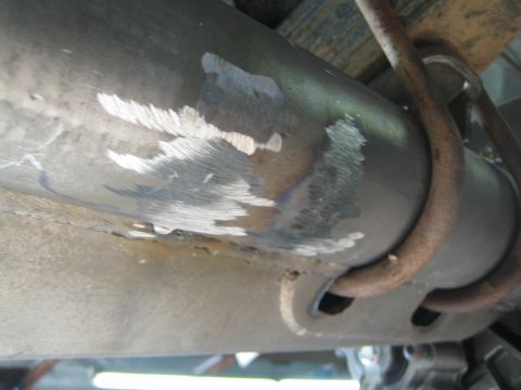 1990 Ford Bronco - close-up of a bare-metal axle housing with grinding and weld marks where a leaf spring and U-bolt attach.