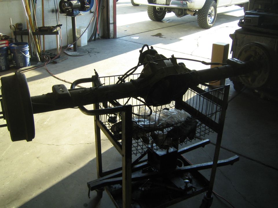 Complete rear axle assembly resting on a wire shop cart in a garage