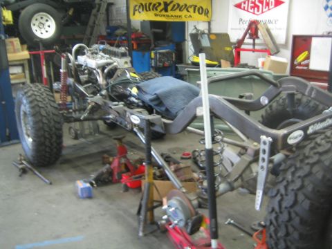 1990 Ford Bronco - bare 4x4 rolling chassis with engine and seats sits mid-build in a shop beneath a FourXDoctor of Burbank banner.