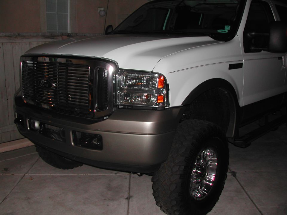 Front 3/4 view of lifted white Ford Excursion with chrome grille and off-road tires at night