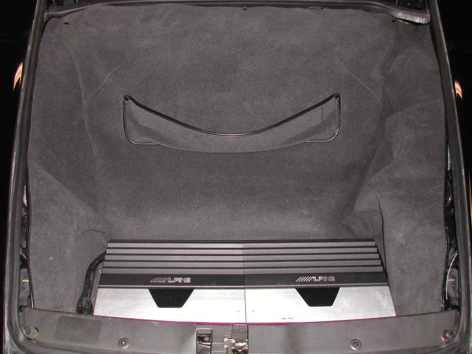Two Alpine amplifiers mounted on aluminum panel in carpeted sports car trunk