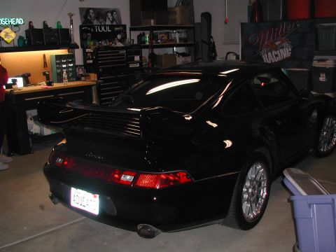 1997 Porsche 911 - Rear view of a black Porsche 911, a prominent spoiler and aftermarket wheels, parked in a garage.