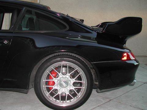 1997 Porsche 911 - Rear view of a black Porsche 911 with a prominent spoiler and multi-spoke wheels.