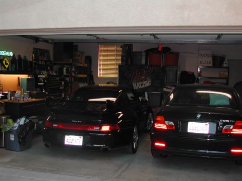 1997 Porsche 911 - A black Porsche 911 with a prominent rear spoiler is parked in a garage next to another car.