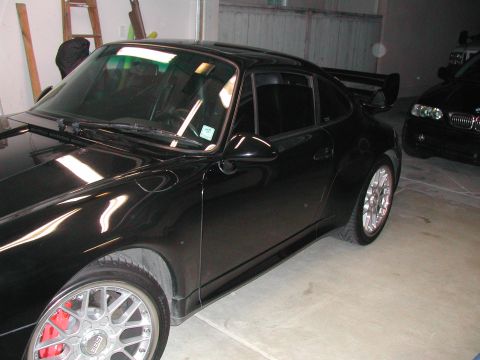 1997 Porsche 911 - A black Porsche 911 with a prominent rear spoiler and aftermarket wheels is parked in a garage next to another vehicle.