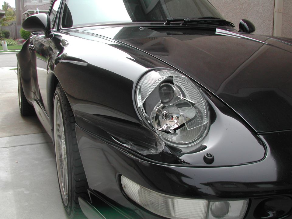 Black Porsche 993 with broken right headlight lens and scraped fender damage, front quarter view