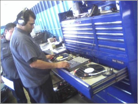 1989 Mazda MX-6 - A man wearing headphones is seen operating turntables in front of a large blue toolbox.
