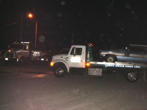 1992 Ford Bronco - Two tow trucks are visible at night, with one truck transporting a light blue car on its flatbed.