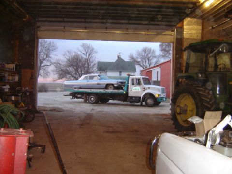 1992 Ford Bronco - A light blue classic car is loaded onto a tow truck inside a garage, with a tractor visible to the right.