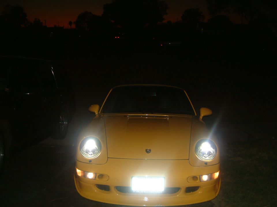 Yellow Porsche 911 front view at night with headlights on