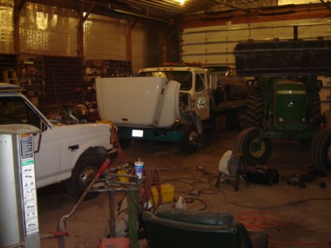 1992 Ford Bronco - Several vehicles, including a truck and a tractor, are parked inside a workshop with the garage door open.