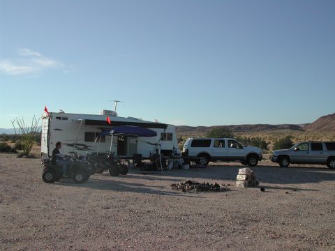 2005 Ford Excursion - A white 2005 Ford Excursion is parked next to a trailer with ATVs, set against a desert backdrop under a clear blue sky.