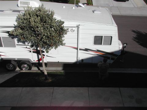 2005 Ford Excursion - A travel trailer is parked in a driveway, partially shaded by a tree. A person is visible near the rear of the trailer.