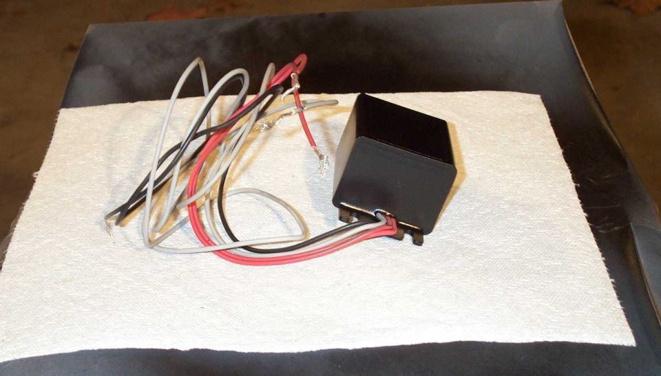 Black electronic tach adapter module with black, white, and red wires on a paper towel.