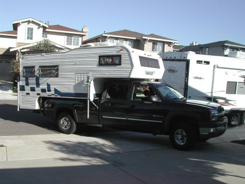 2003 Chevrolet Silverado 2500 - A black 2003 Chevrolet Silverado 2500 pickup truck is parked in a driveway, fitted with a camper shell and adjacent to a white trailer.