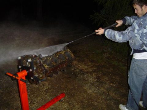 1979 Ford Bronco - A person pressure washes an engine block mounted on an orange engine stand outdoors at night.