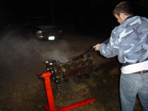 1979 Ford Bronco - Engine block on stand being cleaned with a hose; truck visible in the dark background.