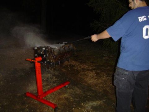 1979 Ford Bronco - A person cleans an engine block outdoors at night with a pressure washer.