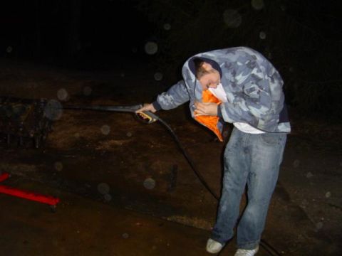 1979 Ford Bronco - person wearing a camouflage hoodie uses a pressure washer on a mechanical part outside at night in rainy conditions.
