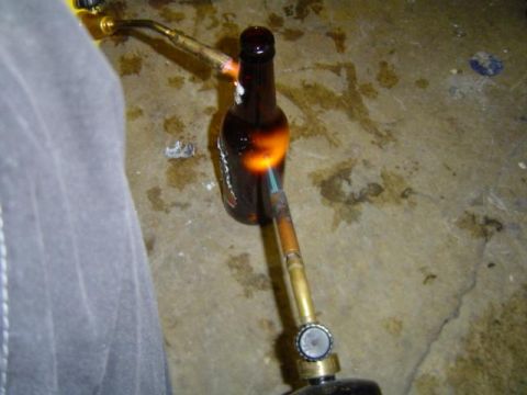 1979 Ford Bronco - A bottle is heated by a torch on a concrete floor with oil stains.