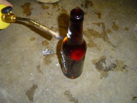 1979 Ford Bronco - Propane torch heating a brown glass bottle on a stained concrete floor.