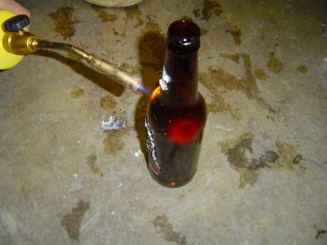 Brown glass bottle being heated by a propane torch on a concrete floor